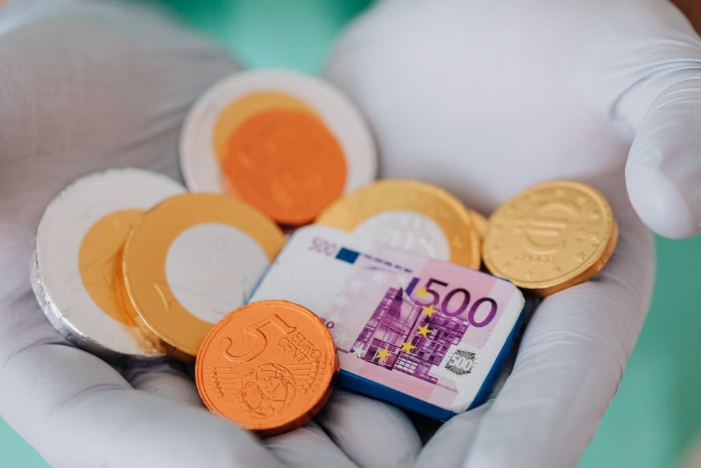 Unrecognizable medical practitioner demonstrating plastic money euro and coins in gloves in clinic while working and holding money wearing medical uniform