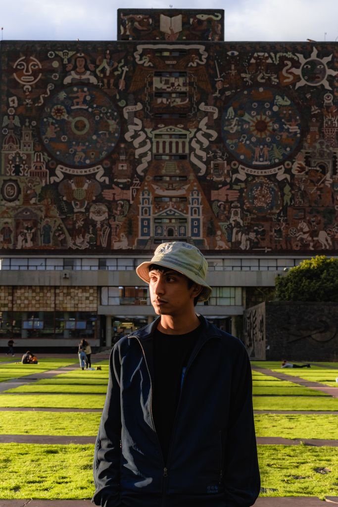 Man wearing a hat stands in front of a richly decorated building facade outdoors.
