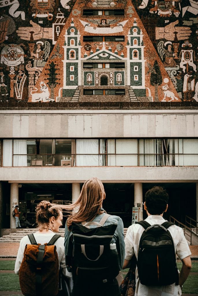 Three young tourists with backpacks admire an elaborate building mural. Urban exploration.